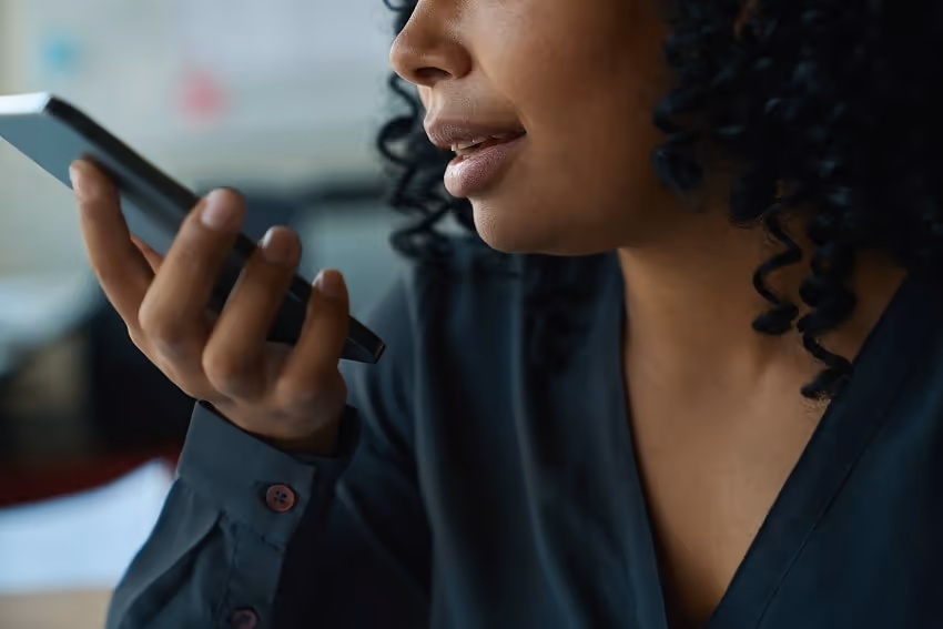 A person holding a smartphone with their mouth near the microphone A person holding a smartphone with their mouth near the microphone