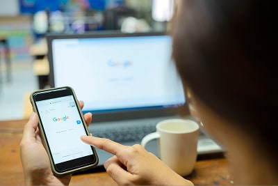 A woman looking at Google on her phone and laptop.