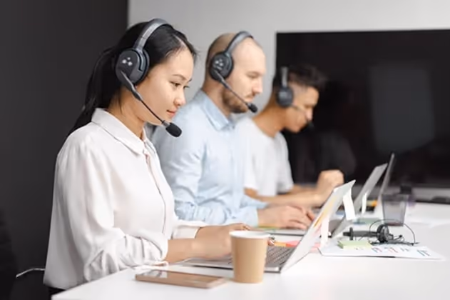 3 people sitting in front of laptops wearing headphones, working in customer service. 3 people sitting in front of laptops wearing headphones, working in customer service.