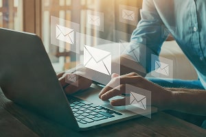 A person working on a laptop who's surrounded by email icons. 