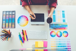 A person sitting at a table drawing surrounded by colourful sample boards.