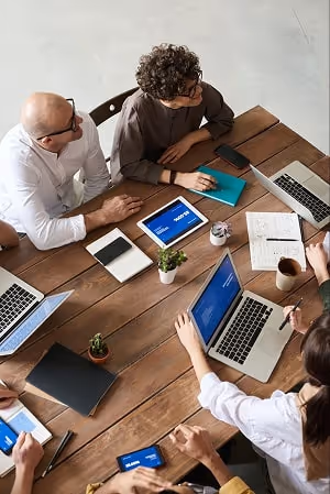 A group of co-workers sitting at a table with notebooks, pens and laptops discussing a certain topic