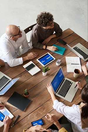 A group of co-workers sitting at a table with notebooks, pens and laptops discussing a certain topic