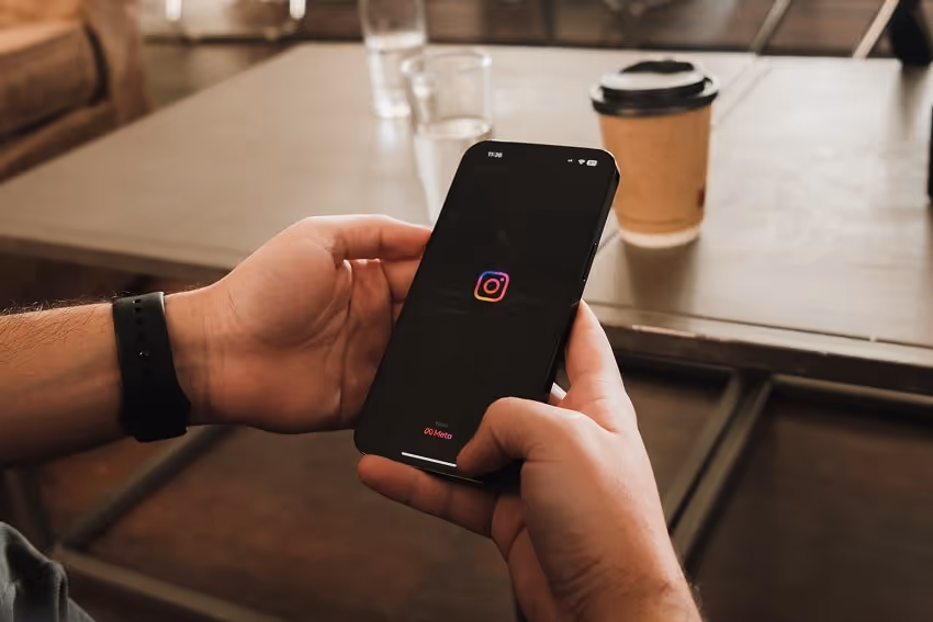 Male hands holding a phone that shows the Instagram logo because the person is opening the app.