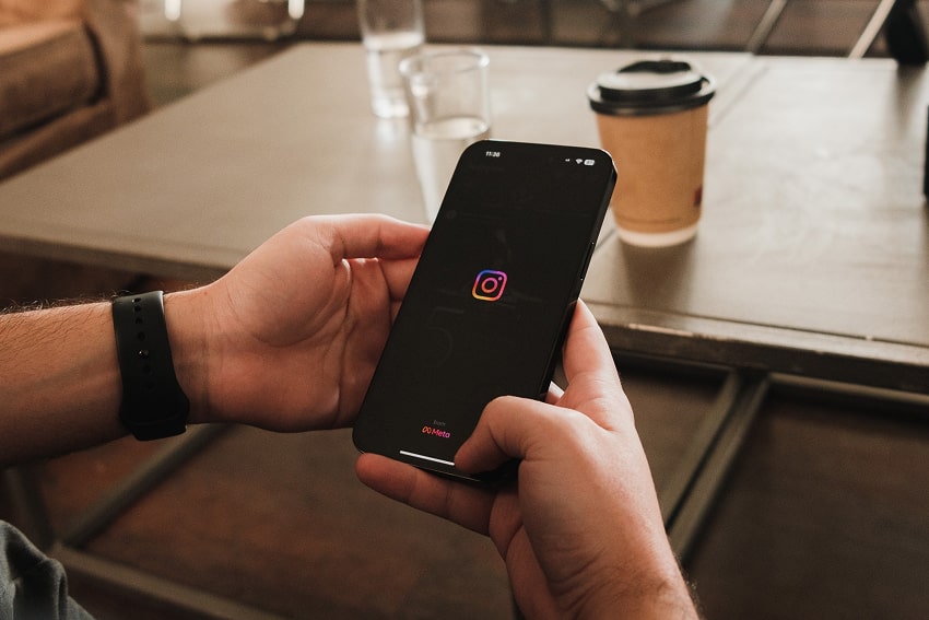 Male hands holding a phone that shows the Instagram logo because the person is opening the app.