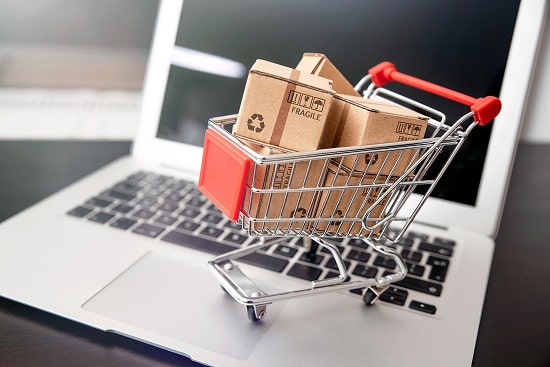 A shopping cart filled with packages stands on a laptop