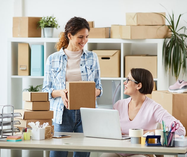 Two people in an office, one standing with a package, the other sitting at a computer