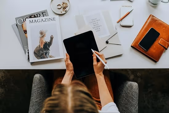 Person using a tablet. Magazines and phone on the desk Person using a tablet. Magazines and phone on the desk