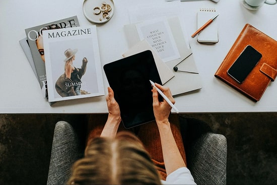 Person using a tablet. Magazines and phone on the desk
