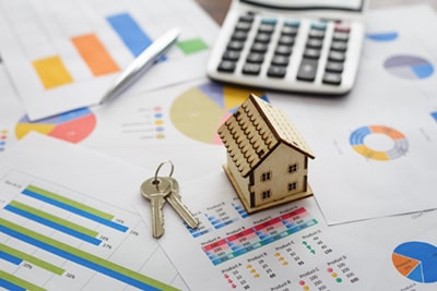 A model house, keys and a calculator placed on top of paperwork which displays graphs and statistics
