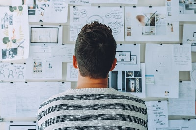 A man standing in front of a white board thinking about what tool to use for calculating revenue.