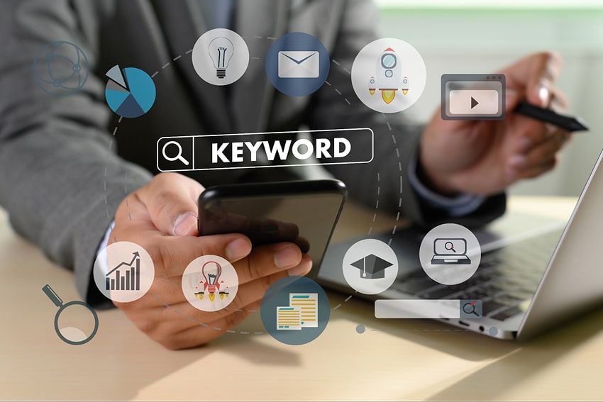 A man looking at his phone and laptop - a search bar showing the word 