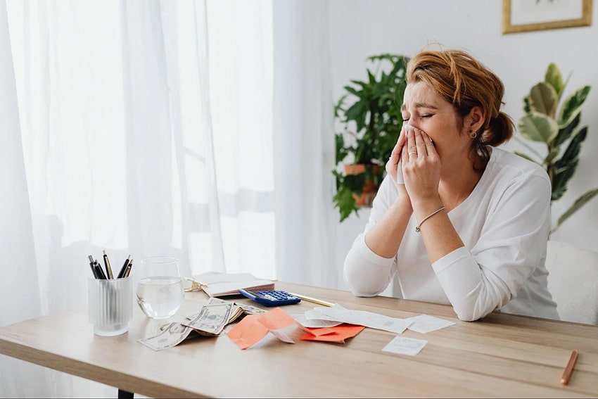 A woman blowing her nose while sitting at a table 