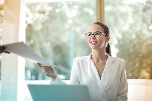 Lady smiling and holding documents. Credit: Andrea Piacquadio.