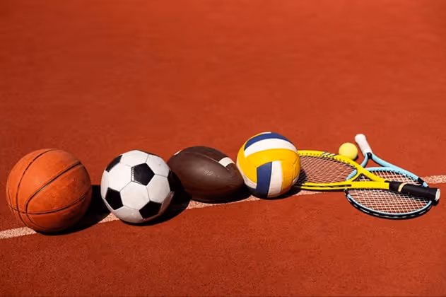 A basketball, soccer ball, football, volleyball, tennis ball, and two tennis rackets neatly placed o A basketball, soccer ball, football, volleyball, tennis ball, and two tennis rackets neatly placed o