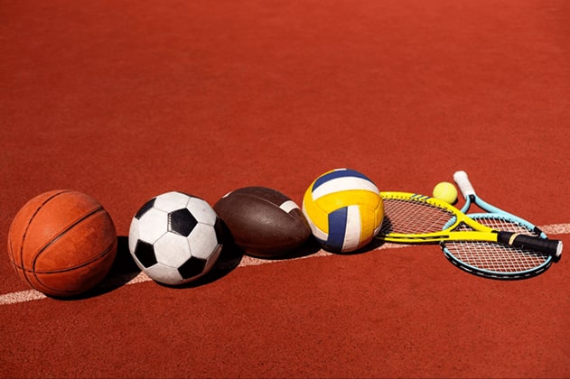A basketball, soccer ball, football, volleyball, tennis ball, and two tennis rackets neatly placed o