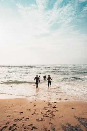 People running from the beach into clear blue water and having fun.