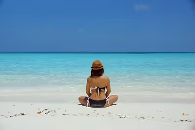 A woman waring a bikini and sitting with her back to the camera on a beach watching the clear blue w A woman waring a bikini and sitting with her back to the camera on a beach watching the clear blue w