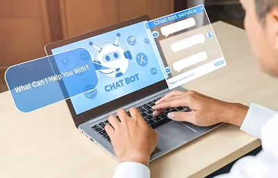 In the image, a man is sitting at a desk with a laptop open in front of him. The man is engaged in t