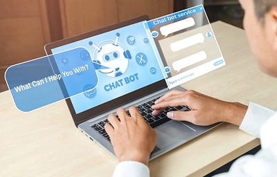 In the image, a man is sitting at a desk with a laptop open in front of him. The man is engaged in t