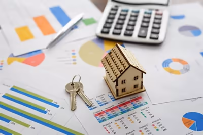 A model house, keys and a calculator placed on top of paperwork which displays graphs and statistics