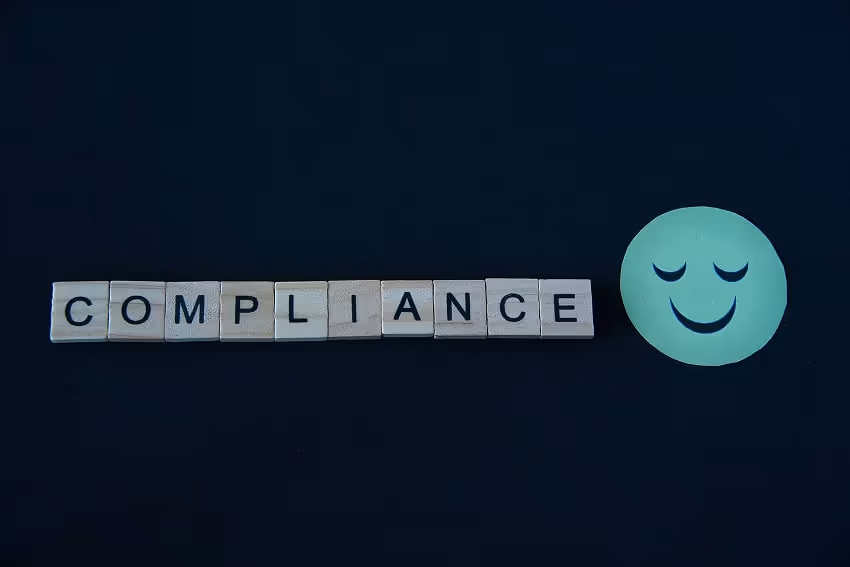 The word Compliance written in wooden letters next to a smiley face The word Compliance written in wooden letters next to a smiley face