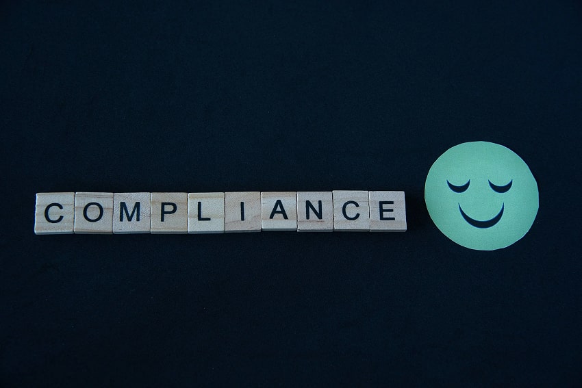 The word Compliance written in wooden letters next to a smiley face
